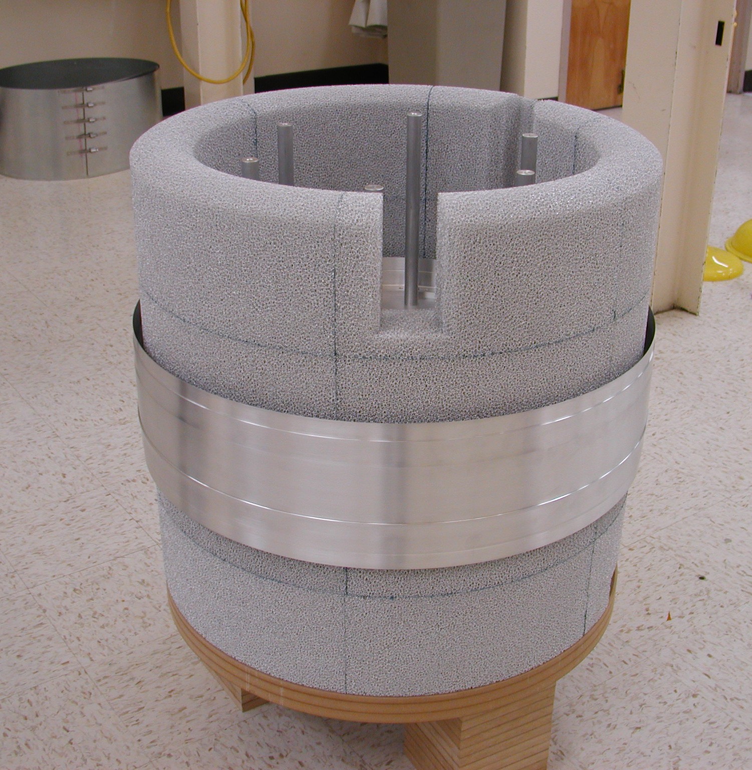 An image of the cyrostat secondary tank's aluminum foam.  Resembles a white-gray covered barrel, with a wide strip of silver-colored, reflective coating around the center.