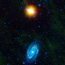 Two distinct galaxies are present in this image.  The top galaxy, Messier 81, is shown as bright orange-yellow.  The bottom galaxy, Messier 81, is shown as bright light blue.